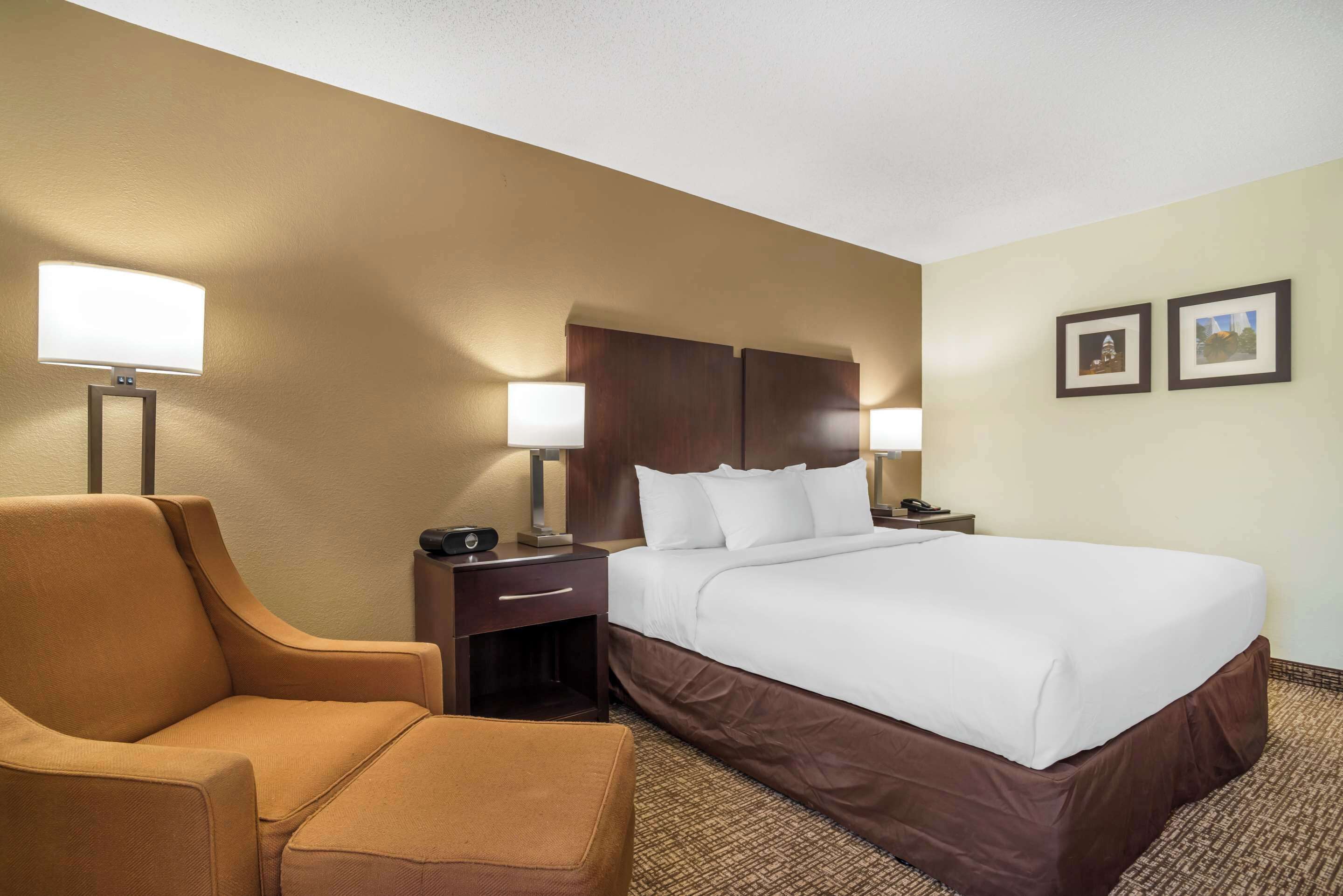A hotel room with a large bed, a chair, two bedside tables with lamps, and two framed pictures on the wall.
