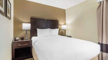 A hotel room with a large bed, two bedside lamps, a nightstand with a clock, and a headboard.