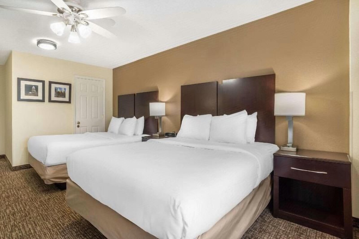 Ein Hotelzimmer mit zwei Betten, einem Deckenventilator, einem Nachttisch mit Lampe und einer Tür mit zwei gerahmten Bildern.