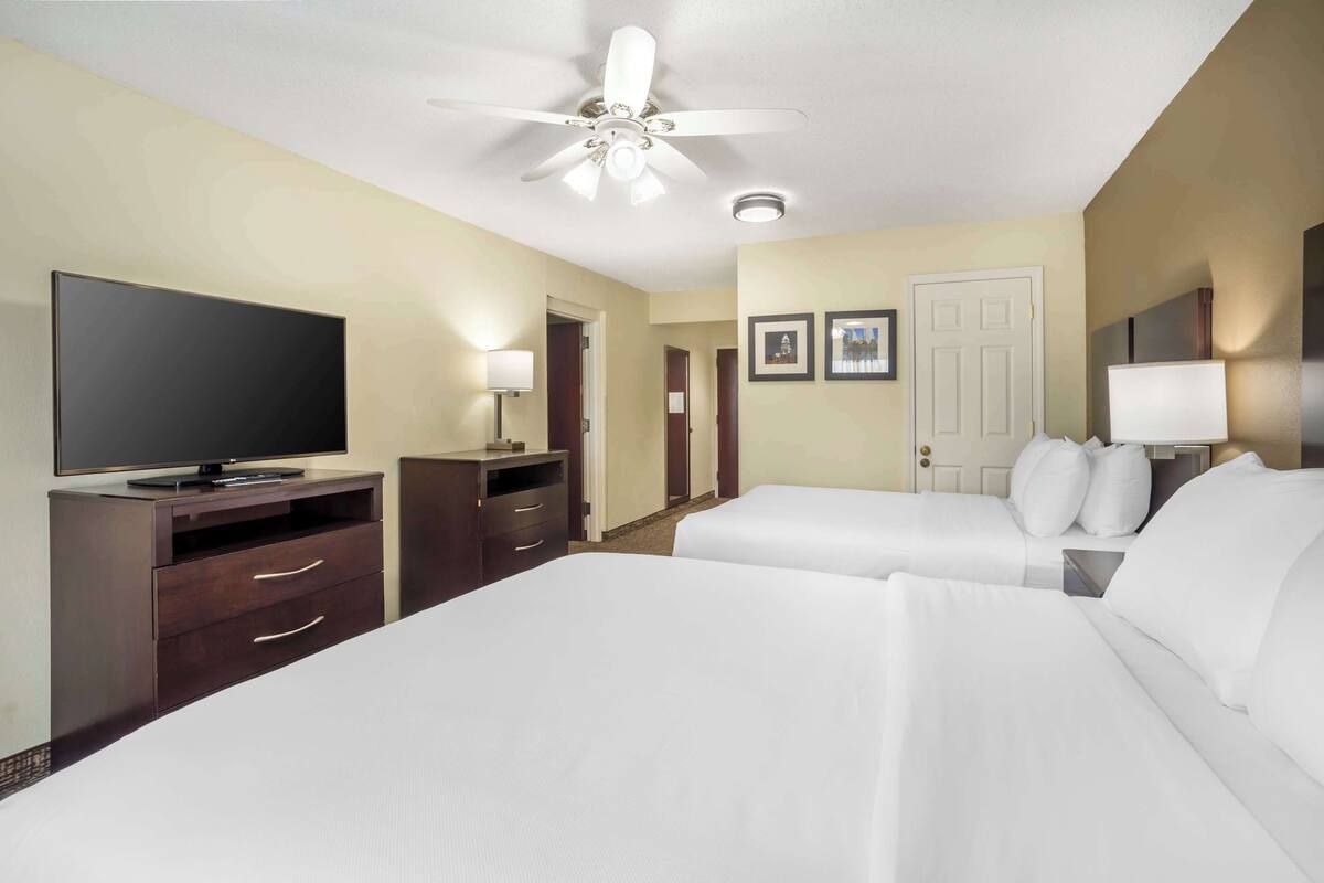A hotel room with two beds, a TV, a desk, and a ceiling fan.