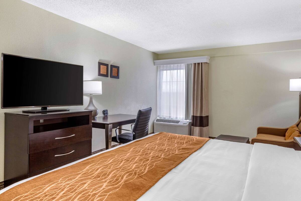 A hotel room with a bed, a desk, a chair, a TV, and a window with curtains.