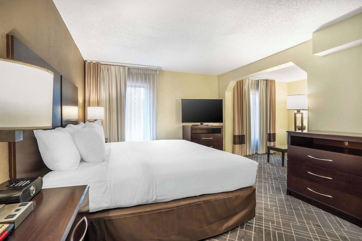 A hotel room with a large bed, a flat-screen TV, a desk with a lamp, and a dresser.