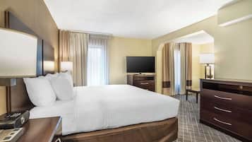 A hotel room with a large bed, a flat-screen TV, a desk with a lamp, and a dresser.