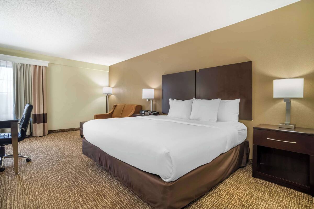 A hotel room with a large bed, two bedside tables with lamps, a desk, and a chair.
