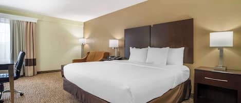 A hotel room with a large bed, two bedside tables with lamps, a desk, and a chair.