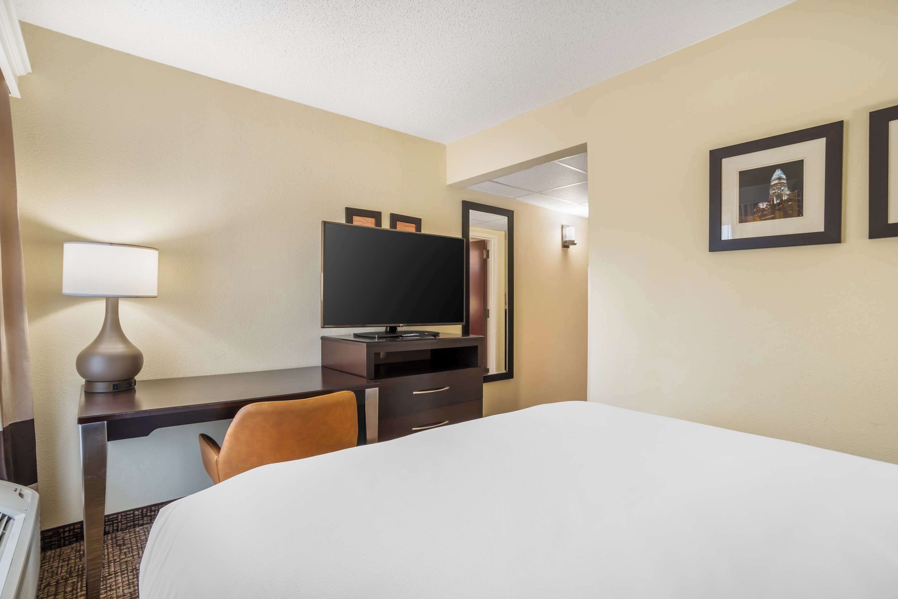 A hotel room with a bed, a desk with a television, a chair, and a lamp.