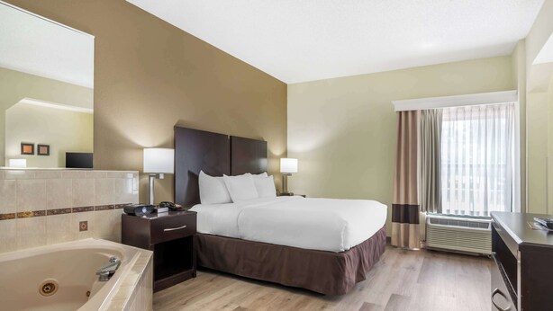 A hotel room with a large bed, a separate bathroom with a bathtub, a desk with a chair, and a window with curtains. - Comfort Inn & Suites Lake Norman (Cornelius)