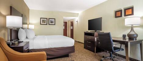 A hotel room with a bed, a desk with a chair, a TV, and a lamp.