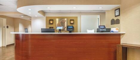 A reception desk with a wooden finish, a digital kiosk, and a framed certificate on the wall.