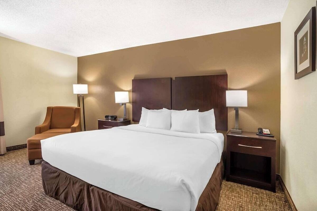A hotel room with a large bed, two bedside tables with lamps, a chair, and a framed picture on the wall.