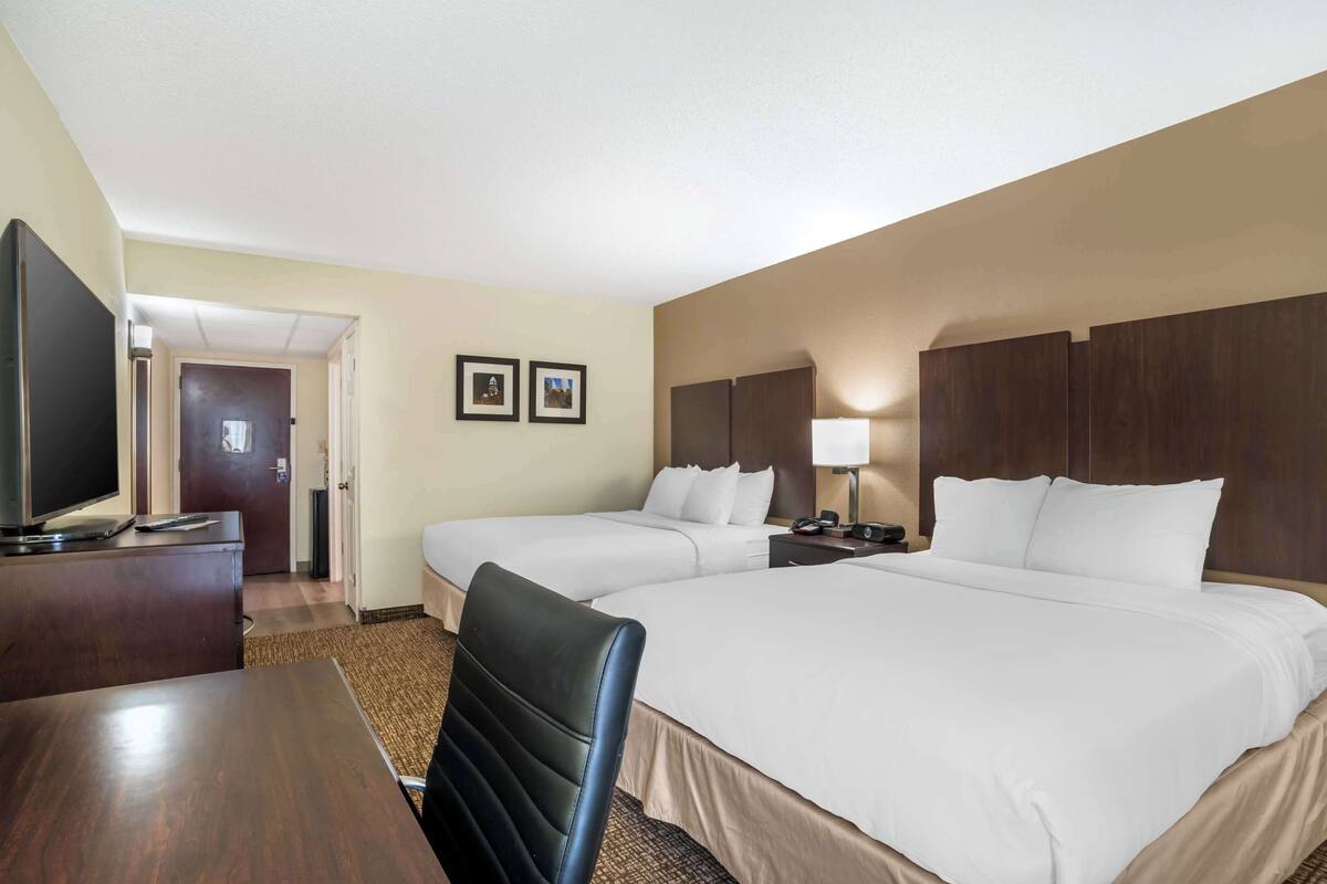 A hotel room with two beds, a desk, a TV, and a door leading to a bathroom.