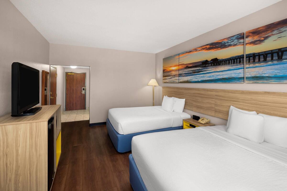 A hotel room with two beds, a TV, a painting of a sunset, and a wooden floor.