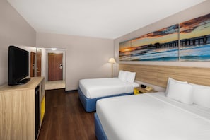 Une chambre d’hôtel avec deux lits, une télévision, un tableau représentant un coucher de soleil et un plancher en bois.