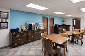Un espace repas avec des tables et des chaises en bois, un comptoir de cuisine équipé d’appareils électroménagers et un mur bleu orné d’œuvres d’art encadrées.