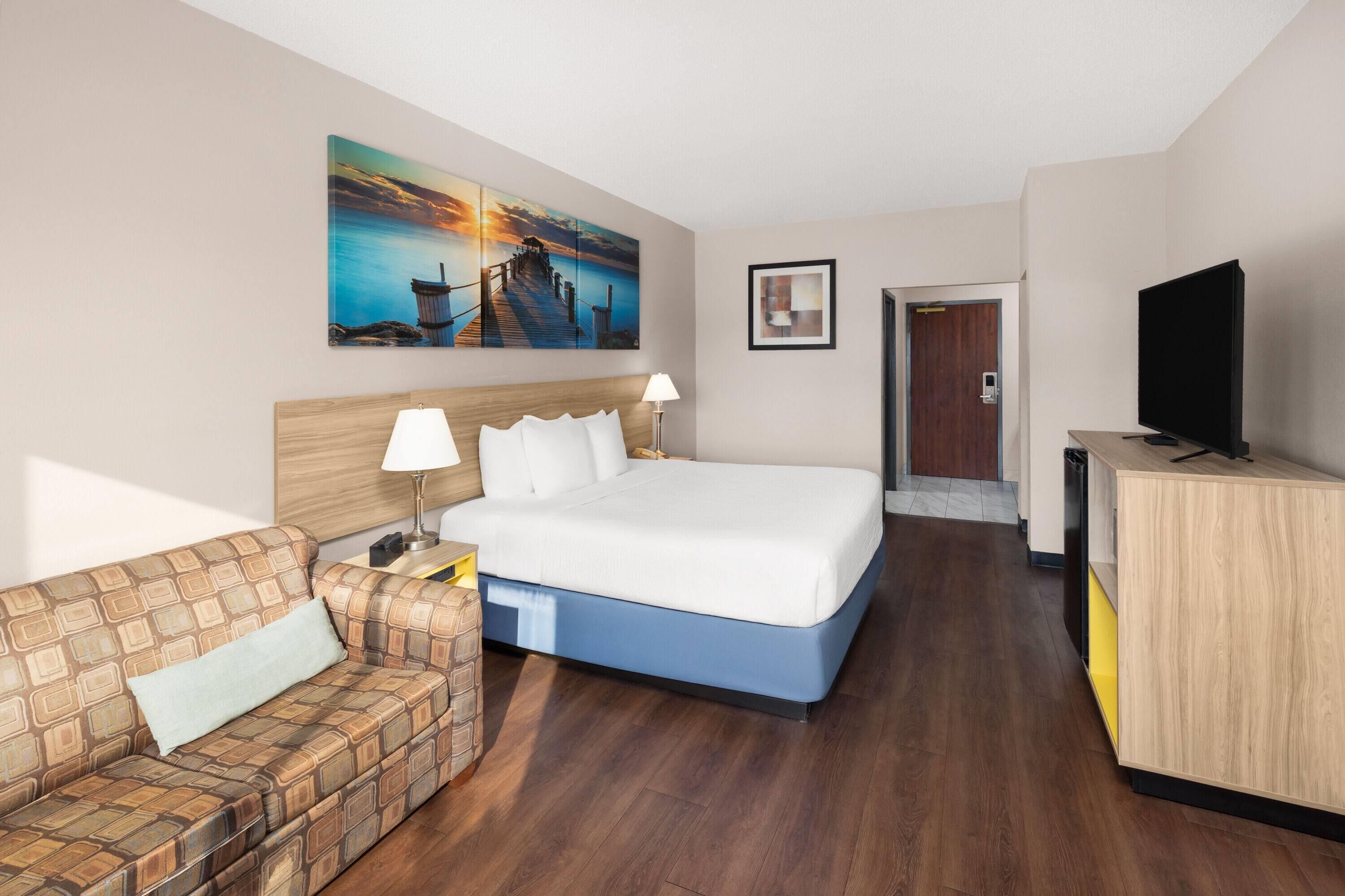 A hotel room with a bed, a TV, a painting, a sofa, and a desk.