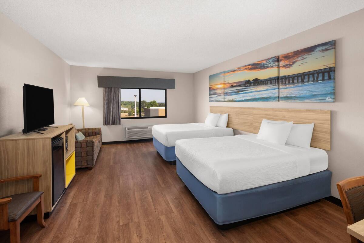 A hotel room with a bed, a desk, a TV, a window, and a painting.