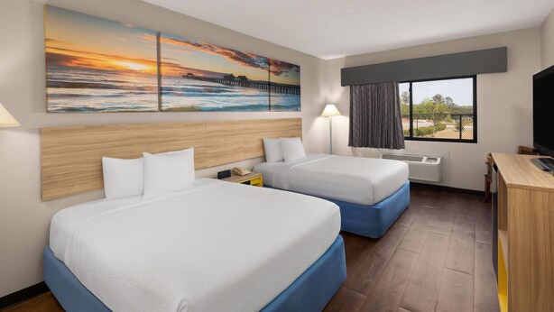 Habitación de hotel con dos camas, un escritorio, un televisor, un cuadro de un atardecer y una ventana con vistas.
