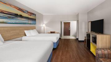 A hotel room with two beds, a TV, a desk, and a painting of a pier.