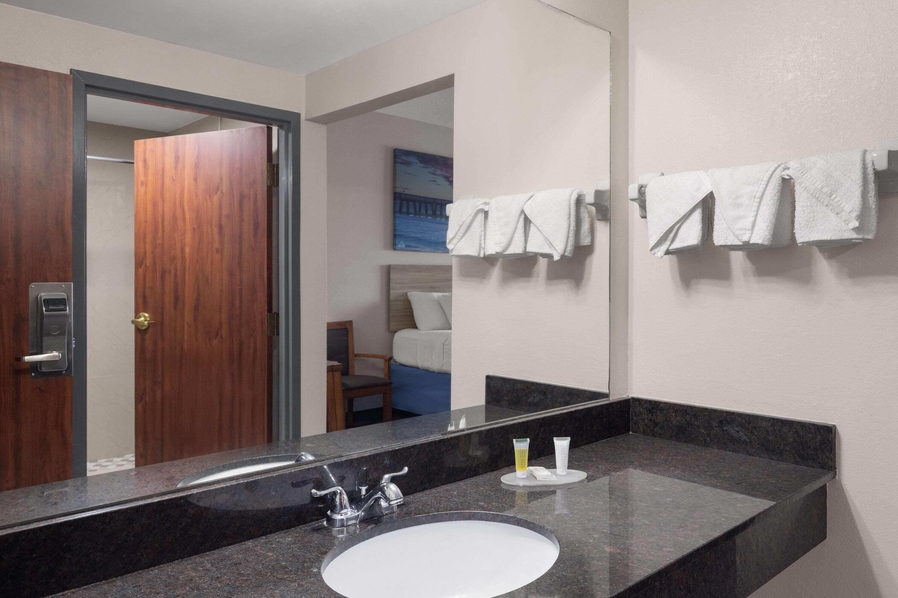 A bathroom with a large mirror, a sink, and towels on a rack.