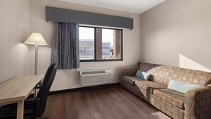 Una habitación con escritorio, silla, sofá, ventana y equipo de aire acondicionado.