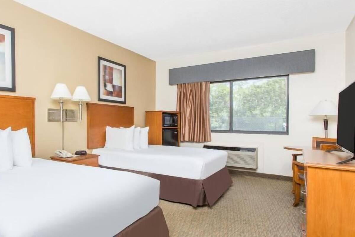 A hotel room with two beds, a desk, a television, and a window with curtains.