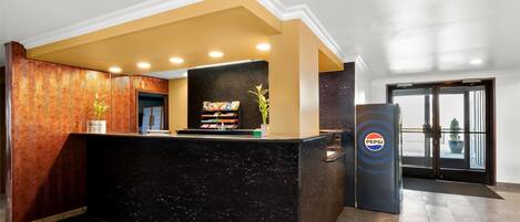 A reception area with a black marble counter, a wooden textured wall, and a Pepsi logo.