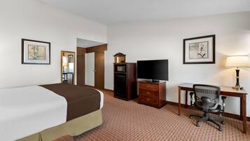 A hotel room with a bed, a desk with a chair, a television, a dresser, and framed artwork on the walls.