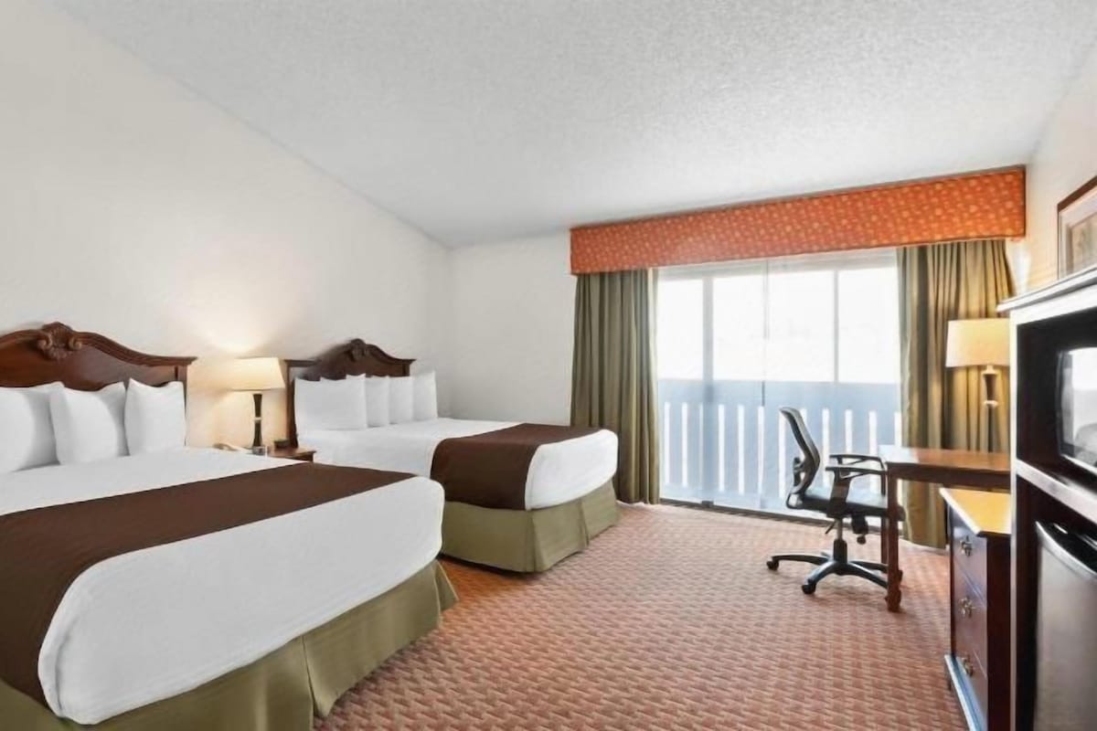 A hotel room with two beds, a desk, a chair, a TV, and a balcony.
