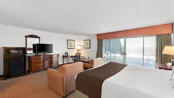 A hotel room with a bed, a desk with a computer, a television, a chair, and a window with curtains.