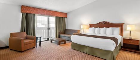 A hotel room with a large bed, a sofa, a chair, a small table, and a nightstand with lamps.