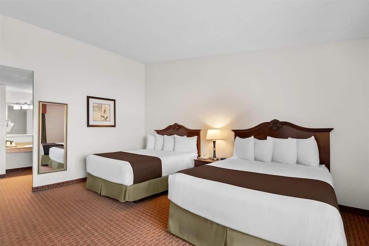 A hotel room with two beds, a mirror, a framed picture, and a nightstand with a lamp.