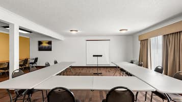 Un salón de conferencias con una larga mesa, sillas, una pantalla de proyector y piso alfombrado.