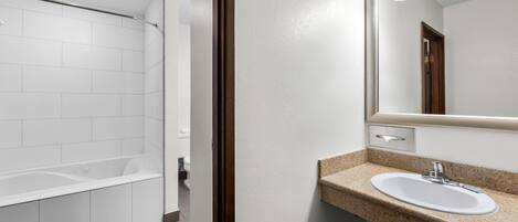 Un baño moderno con una bañera blanca, un lavamanos de granito y un espejo grande con luces arriba.