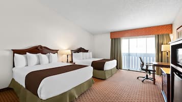 Habitación de hotel con dos camas, un escritorio, una silla y un balcón con vistas.