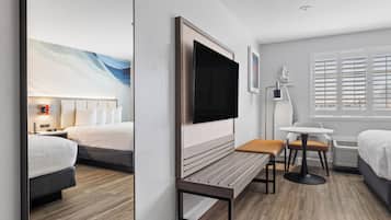 Habitación de hotel con cama, escritorio, silla, televisor y ventana con persianas.