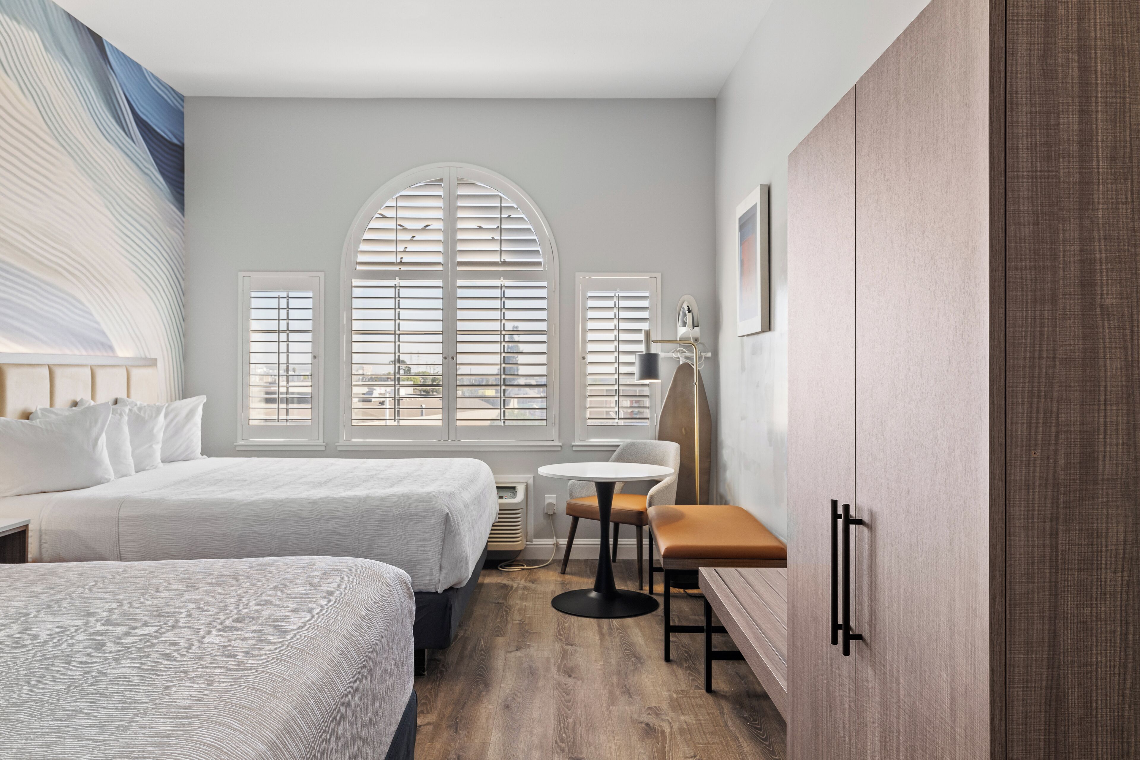 Une chambre d’hôtel avec deux lits, une table ronde, une chaise et une grande fenêtre en arc de cercle.