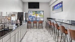 A modern kitchen with marble flooring, a bar area with stools, and a large window offering a view of the street.