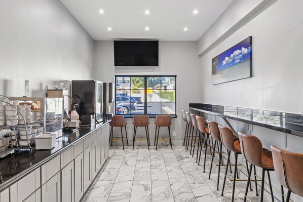 A modern kitchen with marble flooring, a bar area with stools, and a large window offering a view of the street.