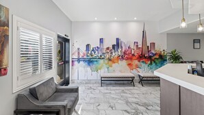 A modern lobby with a cityscape mural, a reception desk, seating area, and a door with blinds.