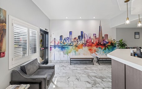 A modern lobby with a cityscape mural, a reception desk, seating area, and a door with blinds.