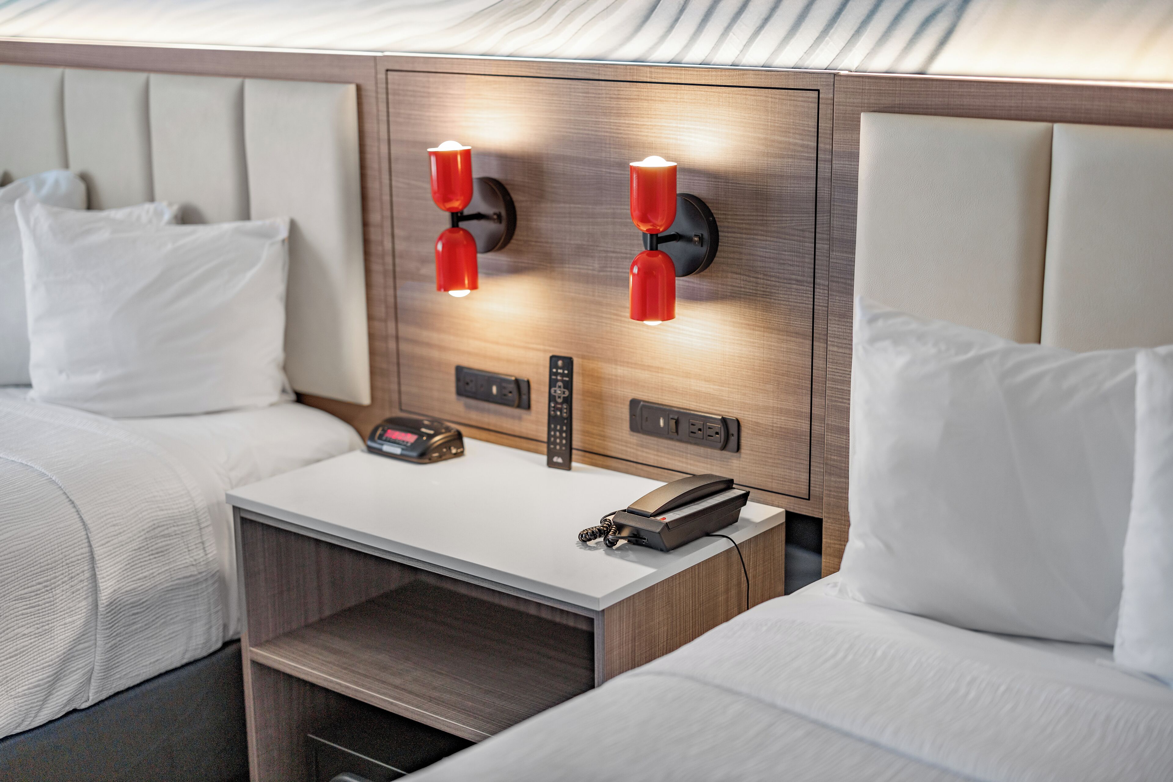 Une chambre d’hôtel avec deux lits, une table de chevet, un téléphone et des lampes fixées au mur.