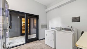 A laundry area with a washing machine and dryer, a sign indicating guest laundry use, and a door leading to a room.