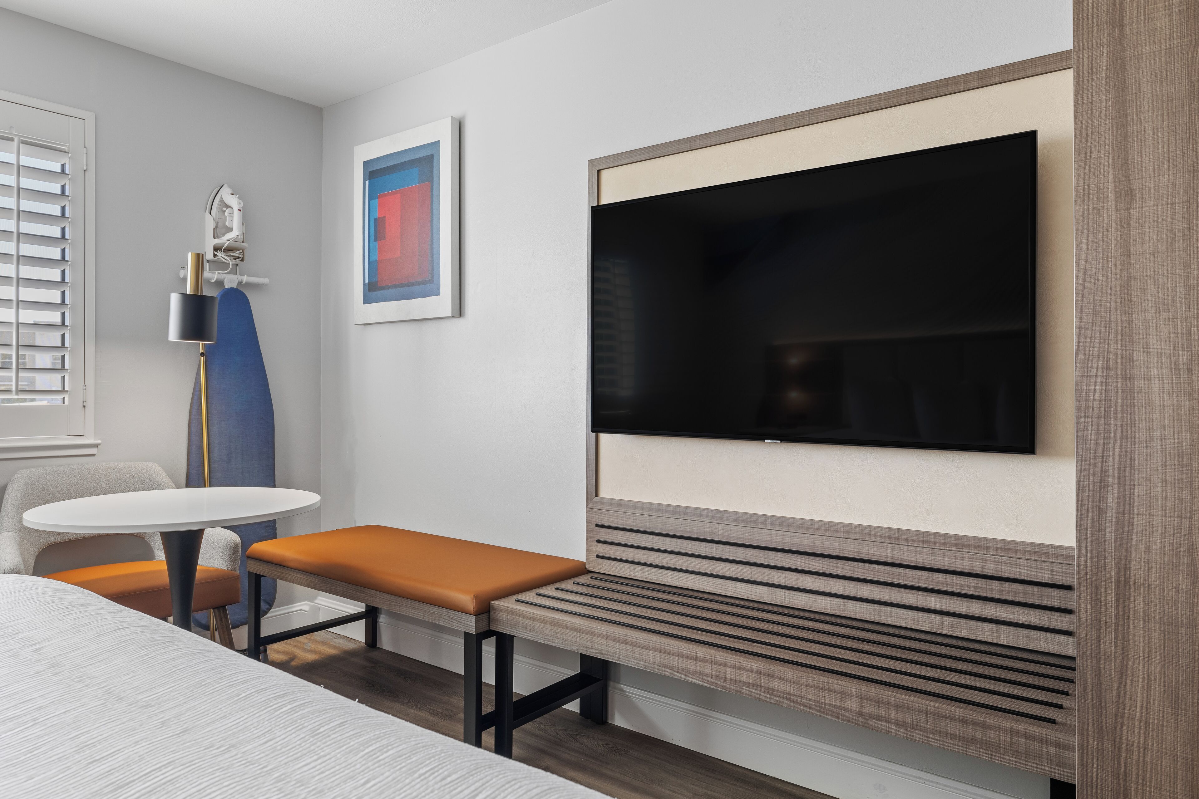 Une chambre d’hôtel moderne dotée d’un grand téléviseur à écran plat fixé au mur, d’une petite table ronde avec un banc et d’un ventilateur de plafond.