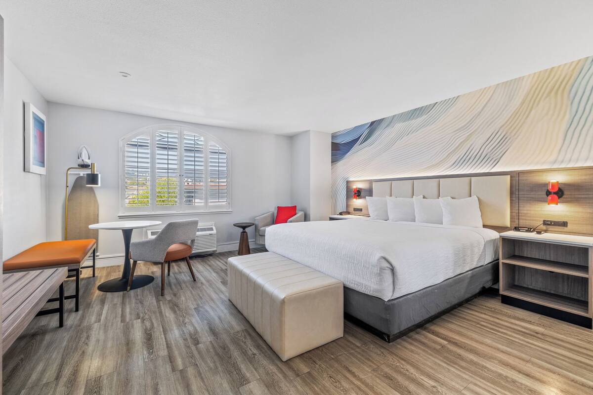 A modern hotel room with a large bed, a desk, a chair, and a bench.