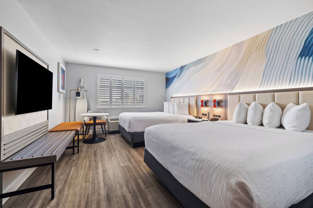A hotel room with a large bed, a desk, a chair, a TV, and a window with blinds.