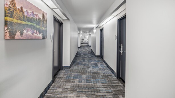 A long, narrow hallway with a patterned carpet, white walls, and doors on both sides.