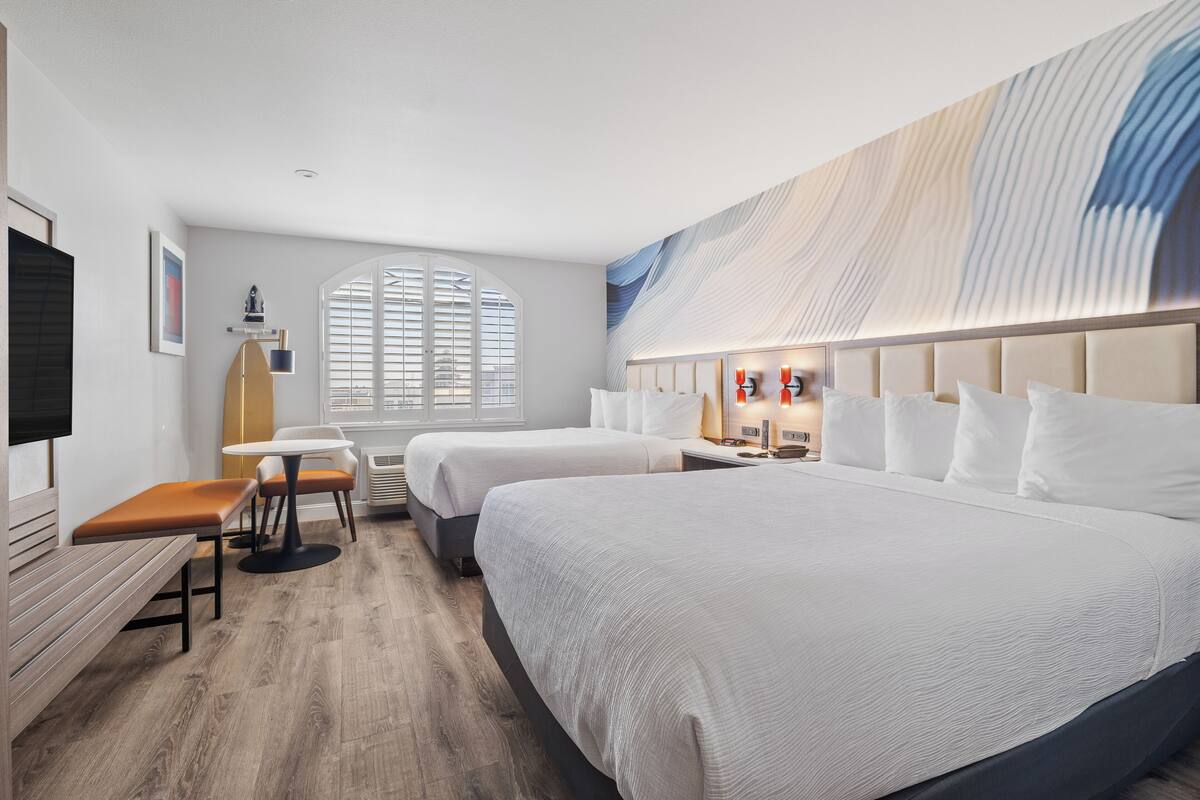 A hotel room with two beds, a desk, and a chair.