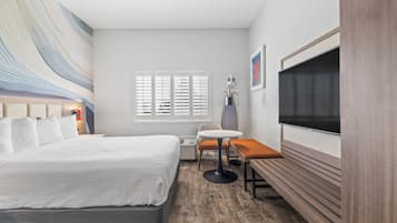 Ett hotellrum med en stor säng, ett litet runt bord, en tv och ett fönster med persienner.
