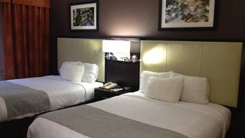 A hotel room with two beds, a nightstand with a lamp, and artwork on the walls.