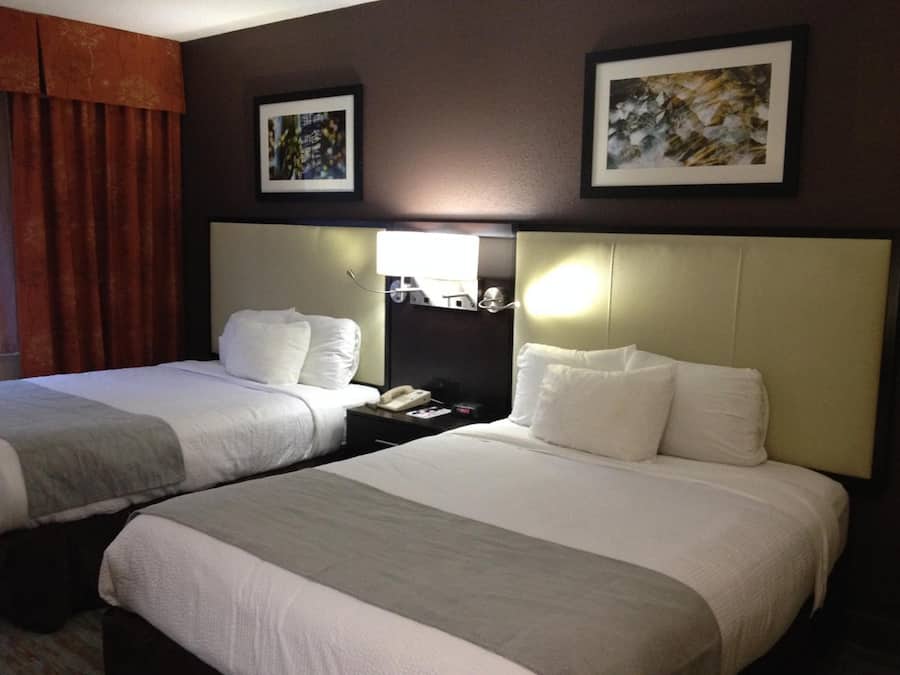 A hotel room with two beds, a nightstand with a lamp, and artwork on the walls.